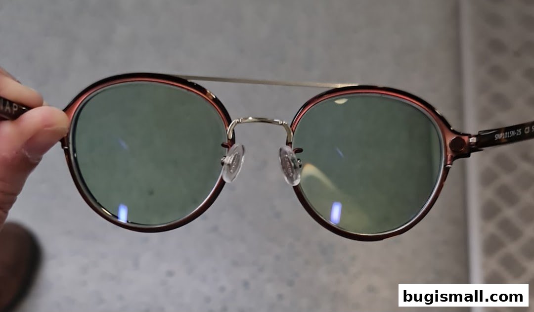 A hand holds a pair of stylish, round-framed glasses with green lenses.