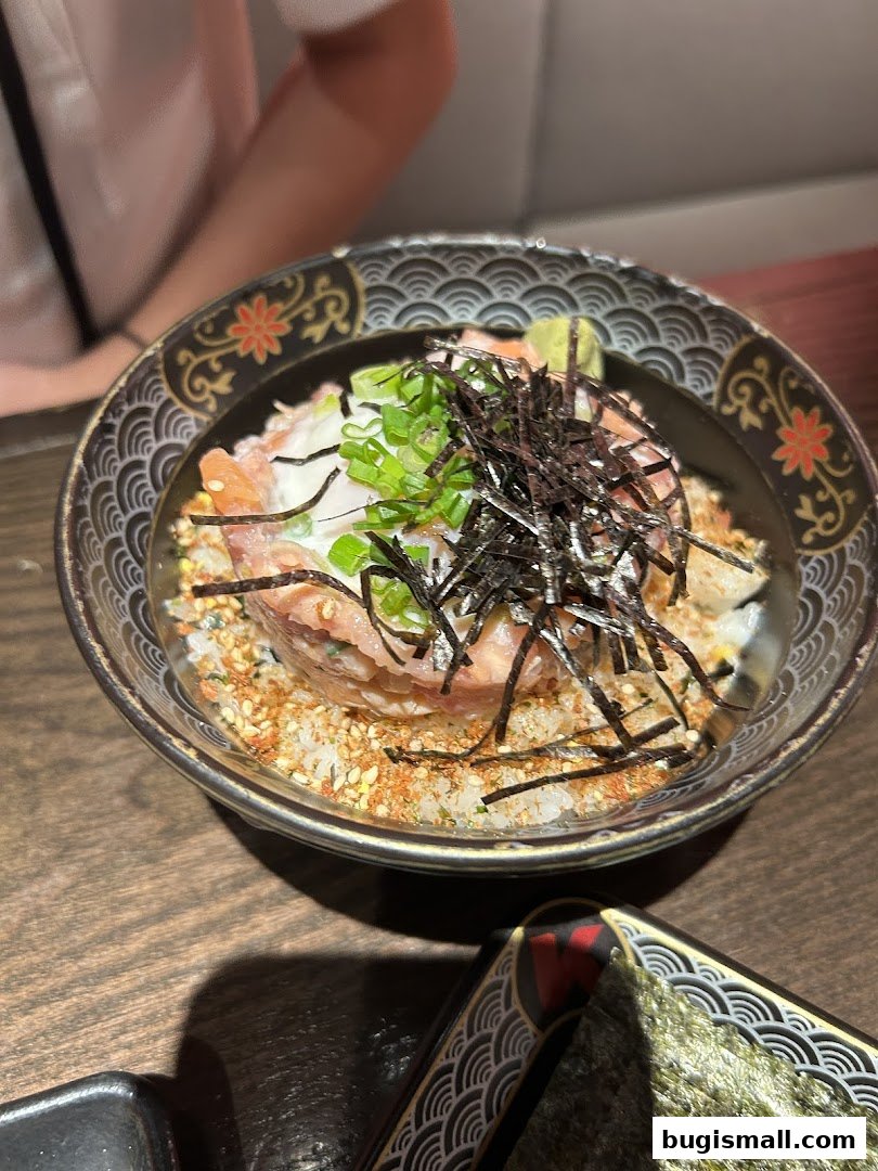 A close-up of a delicious bowl of rice topped with raw fish, green onions, and seaweed.