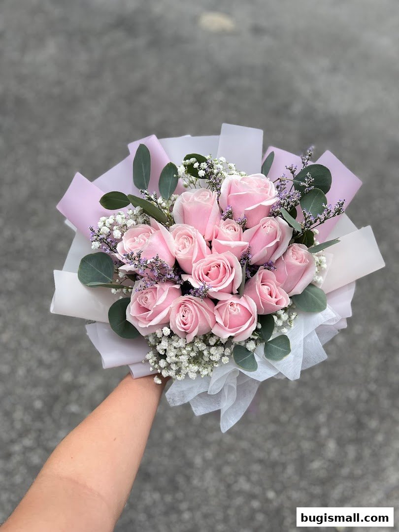 A hand holding a beautiful bouquet of pink roses with baby's breath and eucalyptus.