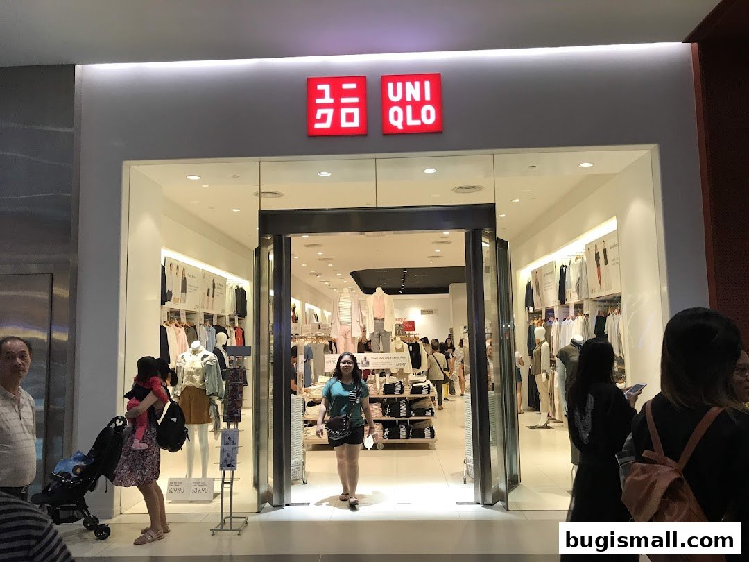 The entrance of a brightly lit Uniqlo store with mannequins displaying clothing and shoppers entering.