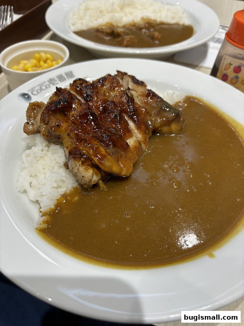 A plate of Japanese curry with grilled chicken and rice, served with a side of corn.