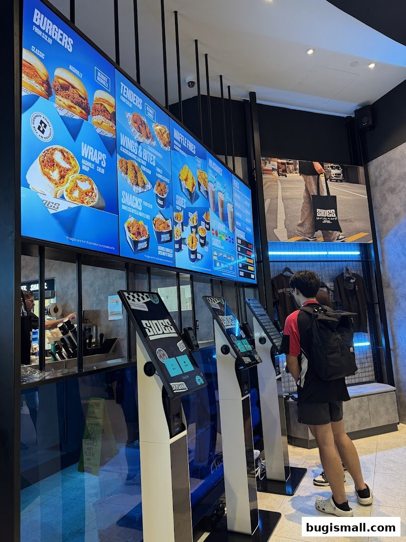 Customers ordering at self-service kiosks in front of a digital menu board at SIDES.