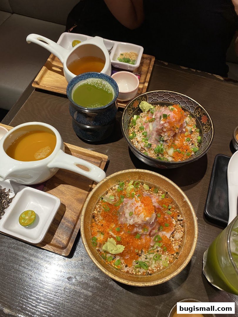 Two bowls of rice topped with fish, roe, and green onions, served with drinks.