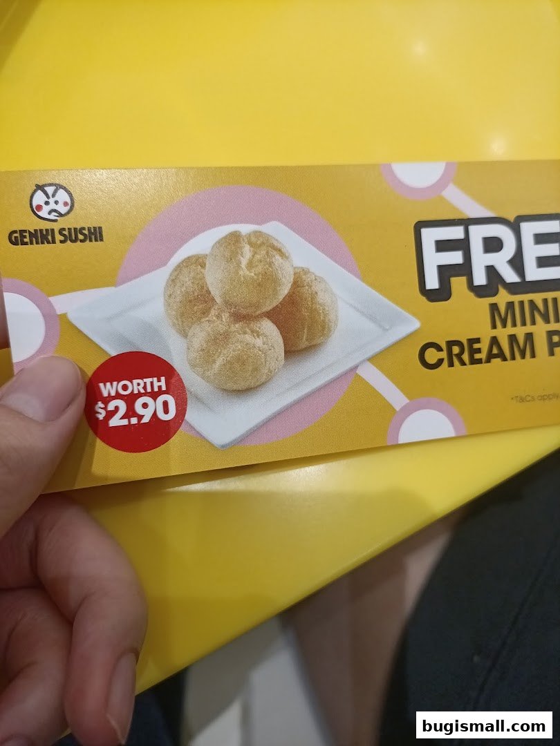 A hand holding a promotional flyer for Genki Sushi featuring mini cream puffs.