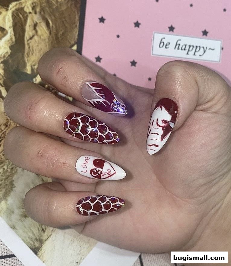A hand with intricately designed stiletto nails featuring red and white patterns, hearts, and glitter.