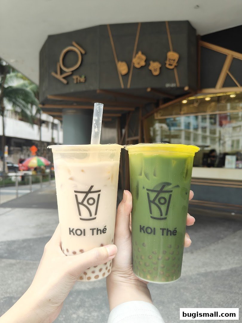 Two hands hold KOI Thé bubble tea drinks, one milk tea and one matcha, in front of the shop.