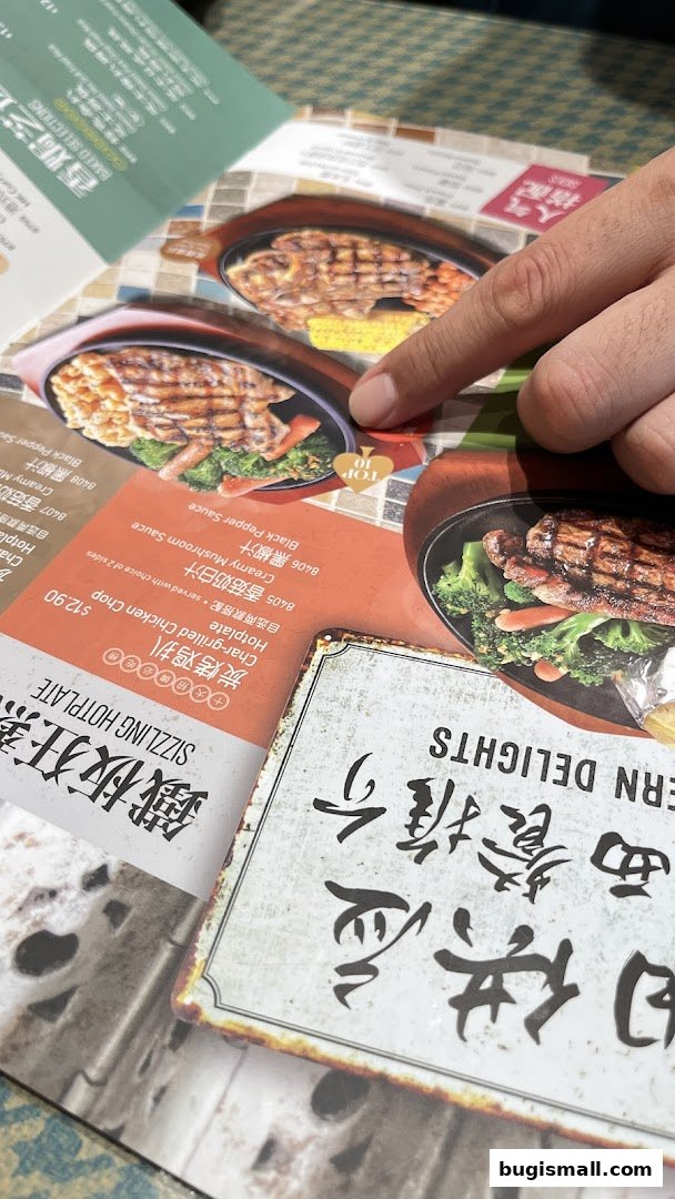 A person's finger points to a menu item at Xin Wang Hong Kong Café, showcasing sizzling hotplates.