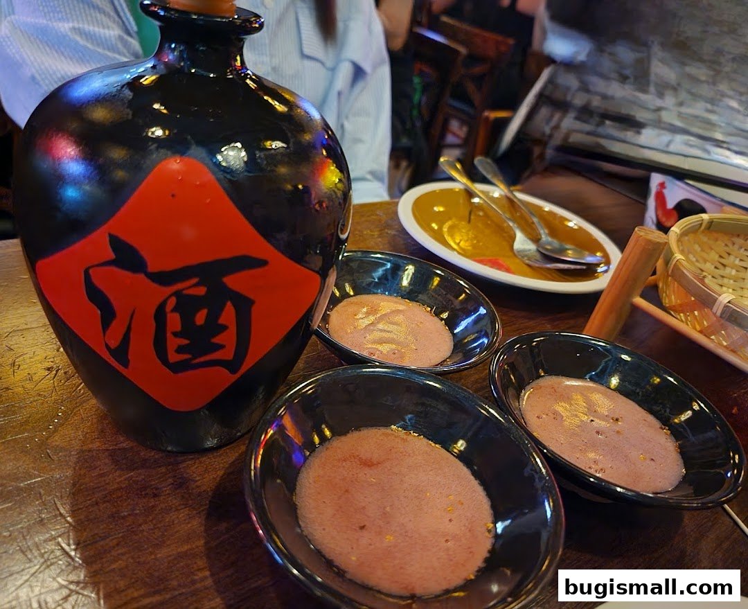 A dark bottle with a red diamond and Chinese characters sits on a wooden table with small bowls of food.