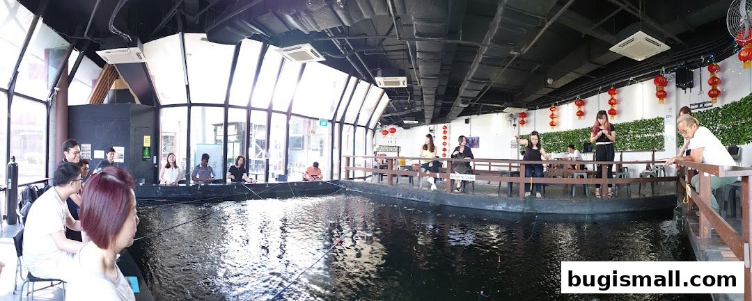 People fishing indoors at a large pond with a wooden deck and decorative lanterns.