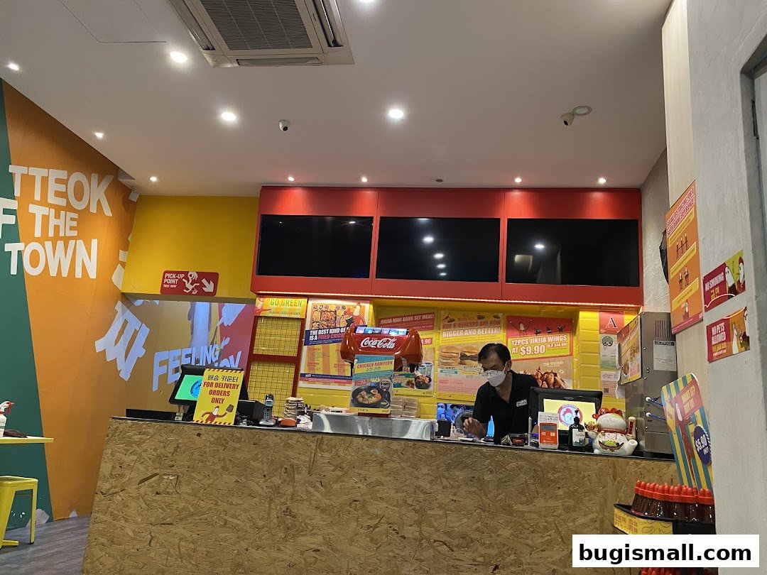Interior of a JINJJA Chicken restaurant with a counter, staff, and menu displays.