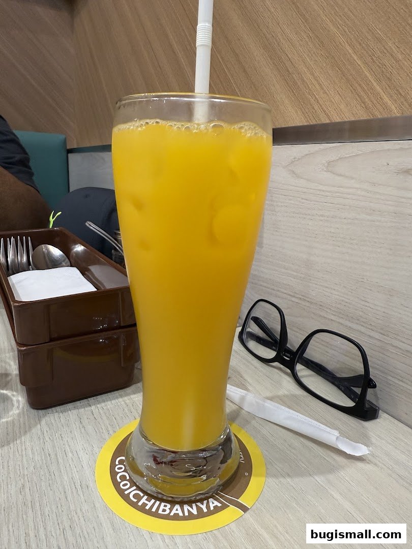A tall glass of orange juice with ice and a straw sits on a coaster.