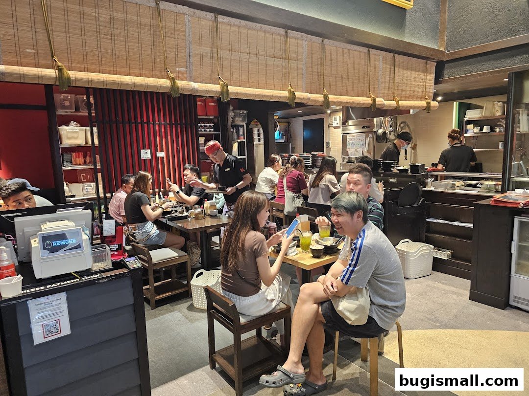 Diners enjoying meals at tables inside a busy Japanese restaurant with staff serving.