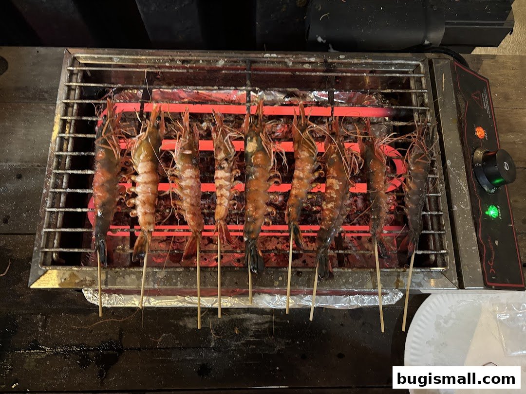 Several large prawns are grilled on skewers over a hot electric grill.