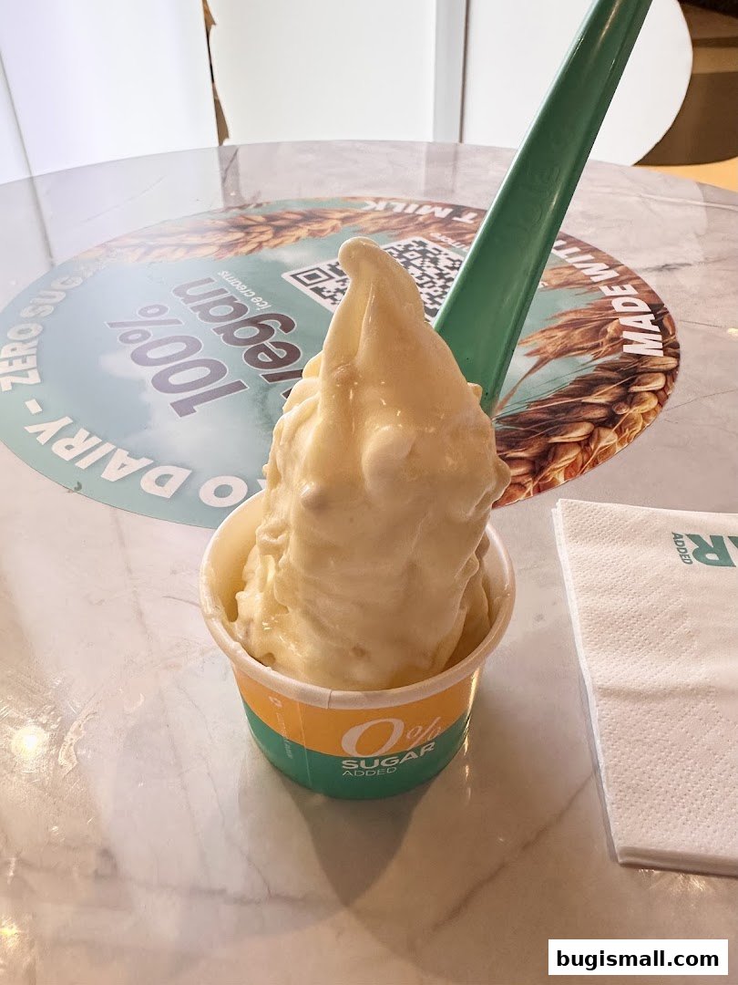 A cup of creamy soft-serve ice cream with a green spoon on a marble table.