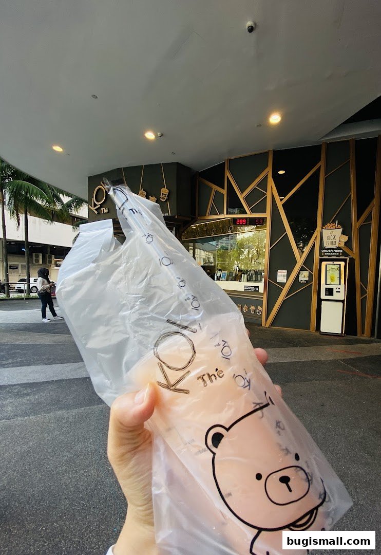 A person holds a KOI Thé drink in a plastic bag in front of the shop.