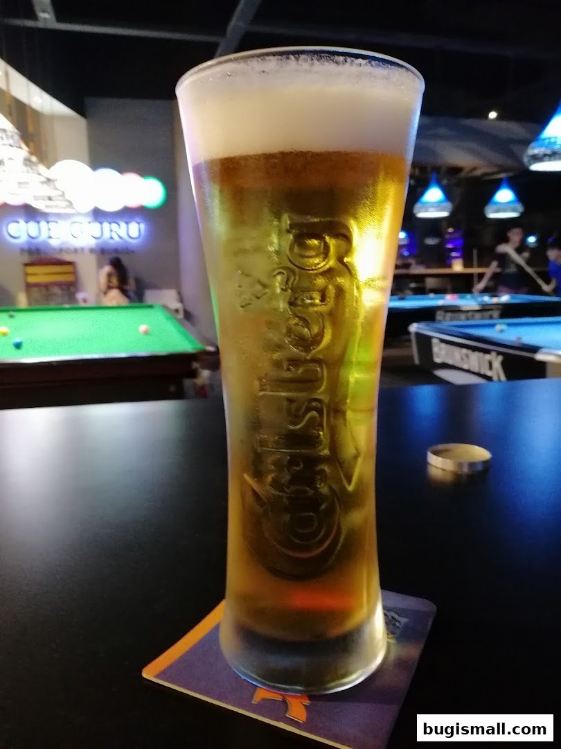 A tall glass of beer sits on a coaster in front of a pool hall.