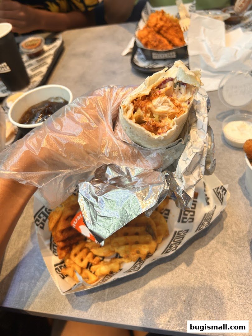 A person holds a chicken wrap and waffle fries from SIDES restaurant.