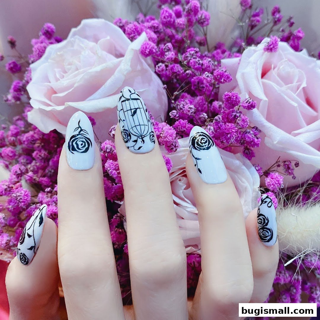 Close-up of hands with white nails featuring black rose and birdcage designs, against a floral backdrop.