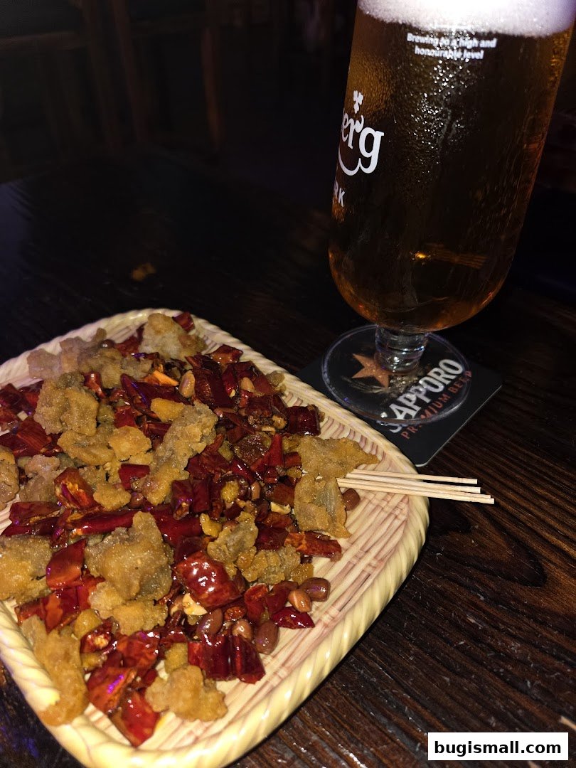 A plate of crispy fried chicken with chili and peanuts next to a glass of beer.