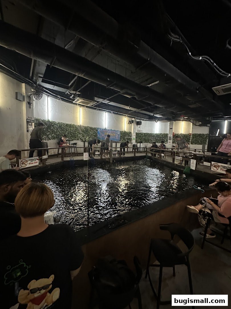People fishing in an indoor pond at Fish Bugis, with seating around the water.