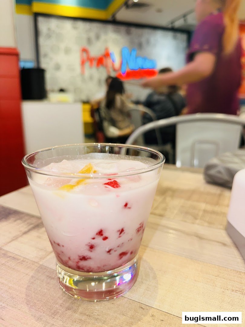 A refreshing pink beverage with fruit pieces and ice in a glass on a wooden table.