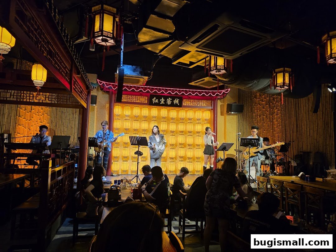 A live band performs on stage at The Inn Livehouse Bugis, with audience members seated at tables.