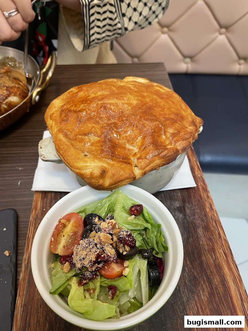 A golden-brown pot pie with a side salad featuring lettuce, tomatoes, olives, and cranberries.