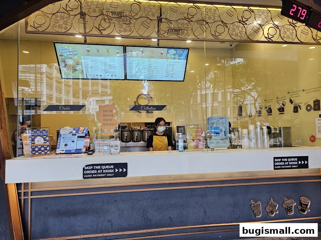 A KOI Thé counter with staff serving customers and digital menus displaying drinks.