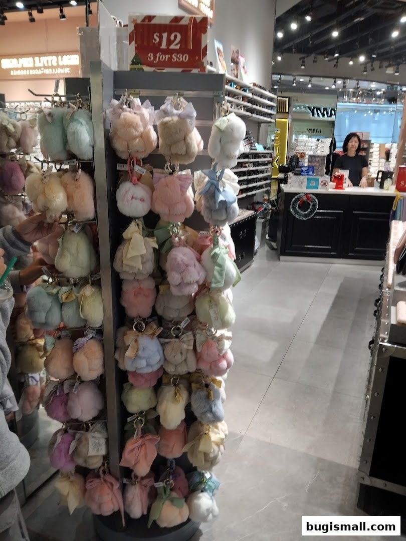 A display of fluffy keychains in various pastel colors, with a promotional sign and a store counter in the background.