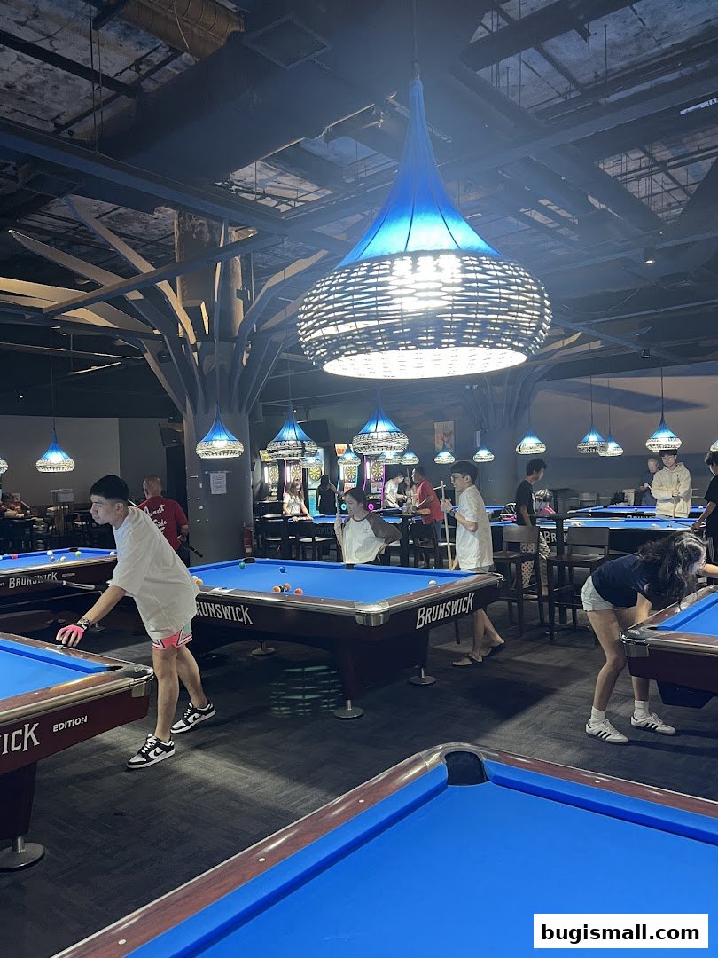 People playing pool in a dimly lit venue with blue lighting and modern decor.