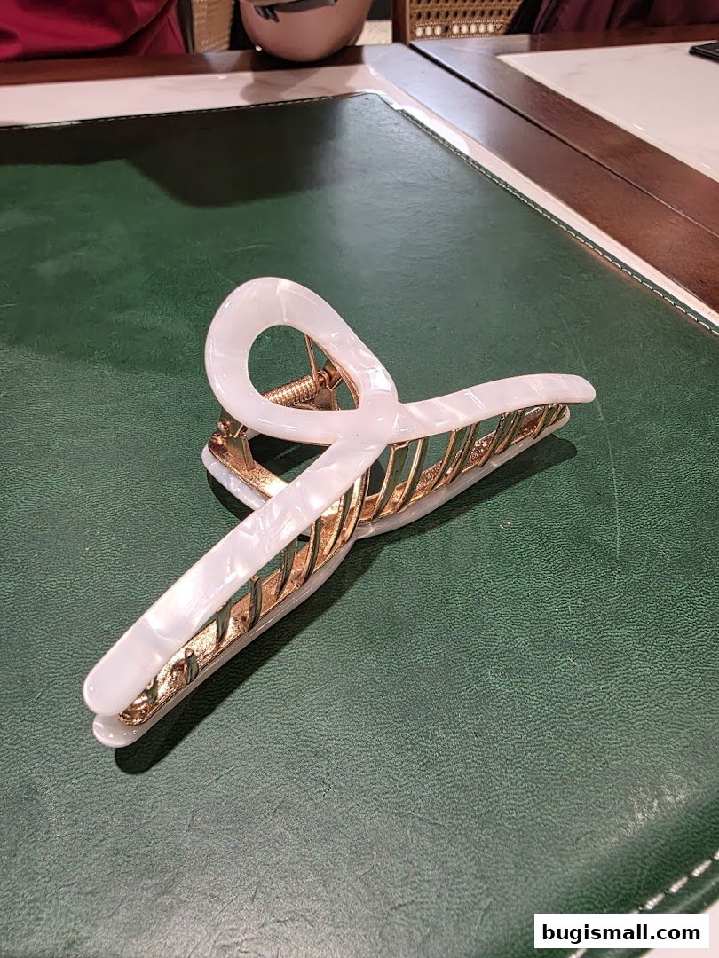 A stylish white and gold hair claw clip rests on a green textured surface.