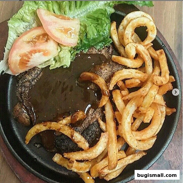 A sizzling steak served with curly fries, lettuce, and tomato slices on a hot plate.