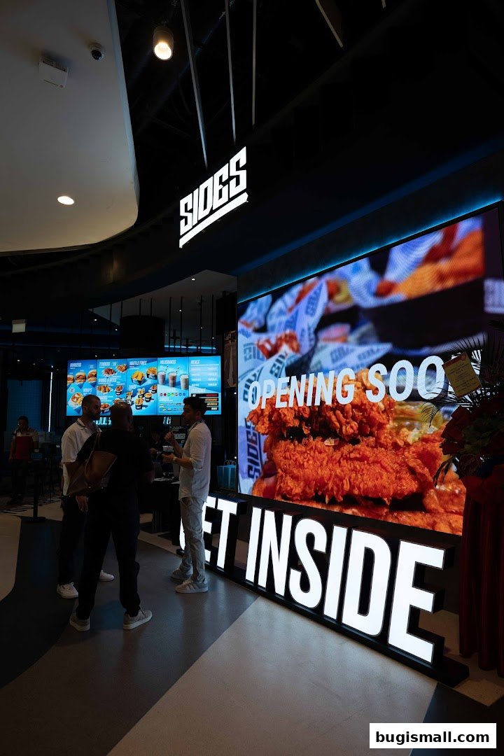 People standing in front of a SIDES restaurant with a large screen displaying food and 'Opening Soon'.