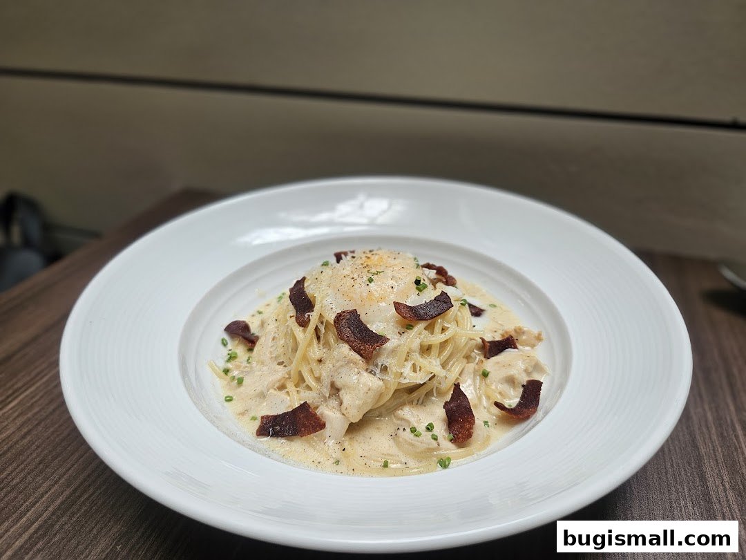 A creamy pasta dish with chicken, bacon, and a poached egg, served in a white bowl.