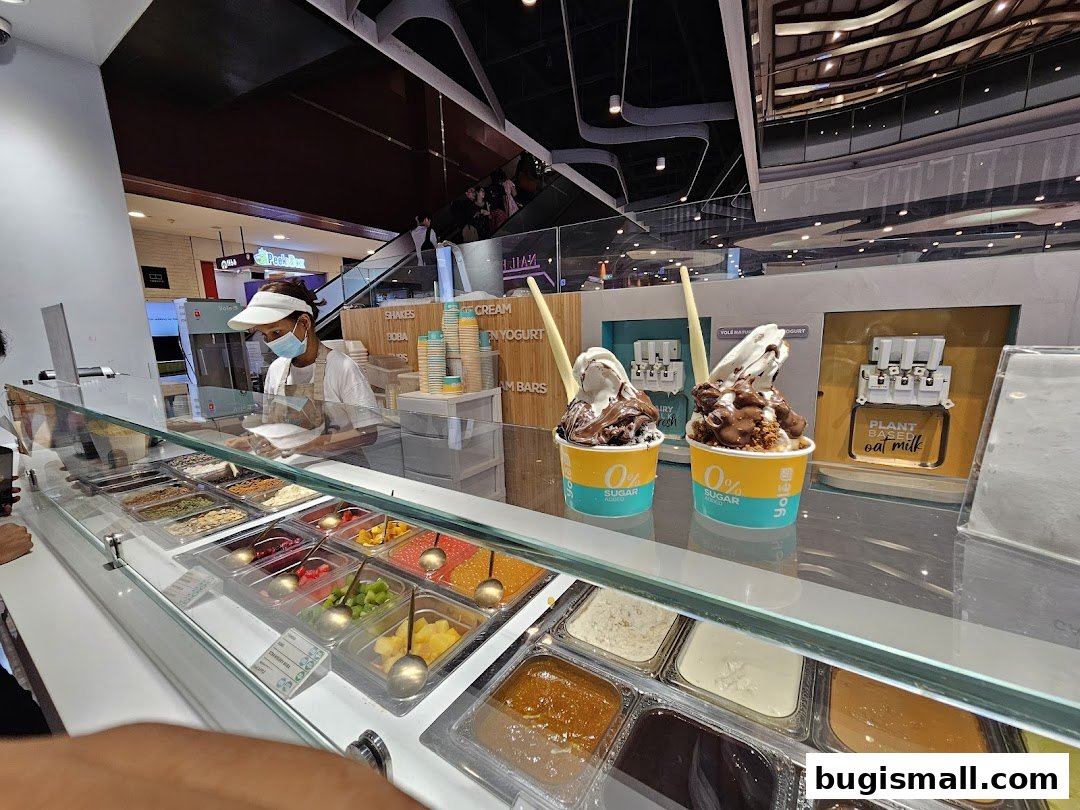 A Yolé shop counter with frozen yogurt, toppings, and a staff member preparing an order.