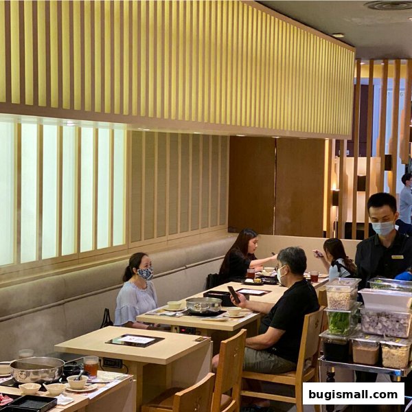Diners enjoy shabu-shabu at tables in a modern restaurant with warm lighting.