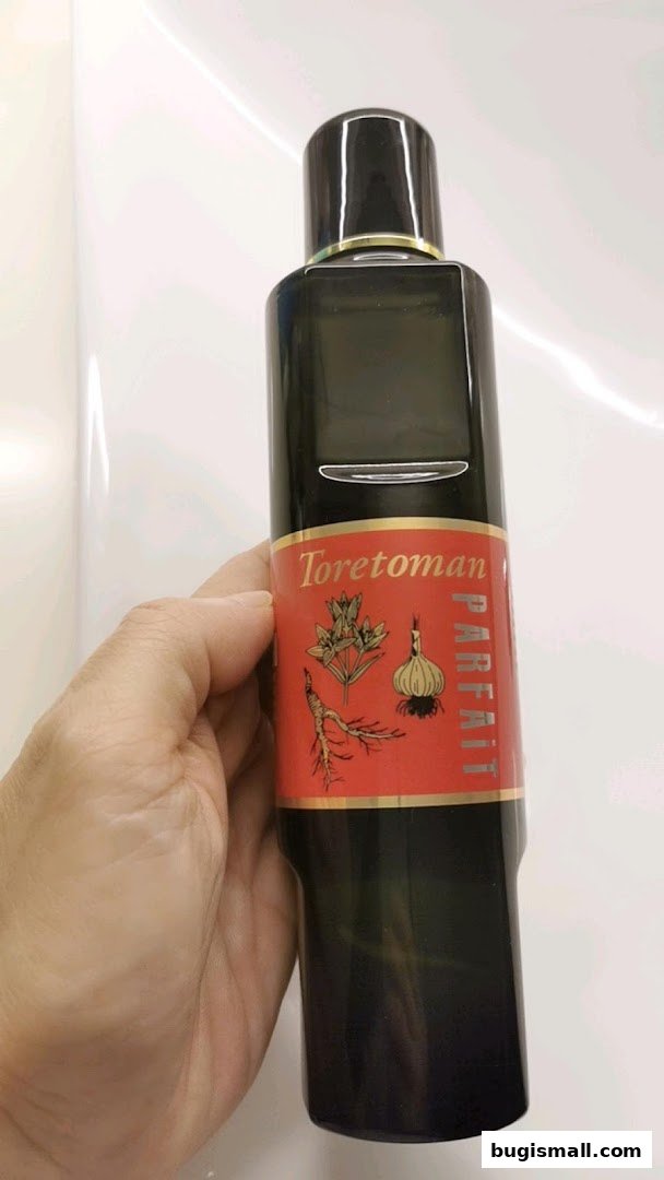 A hand holds a dark glass bottle with a red label featuring botanical illustrations.