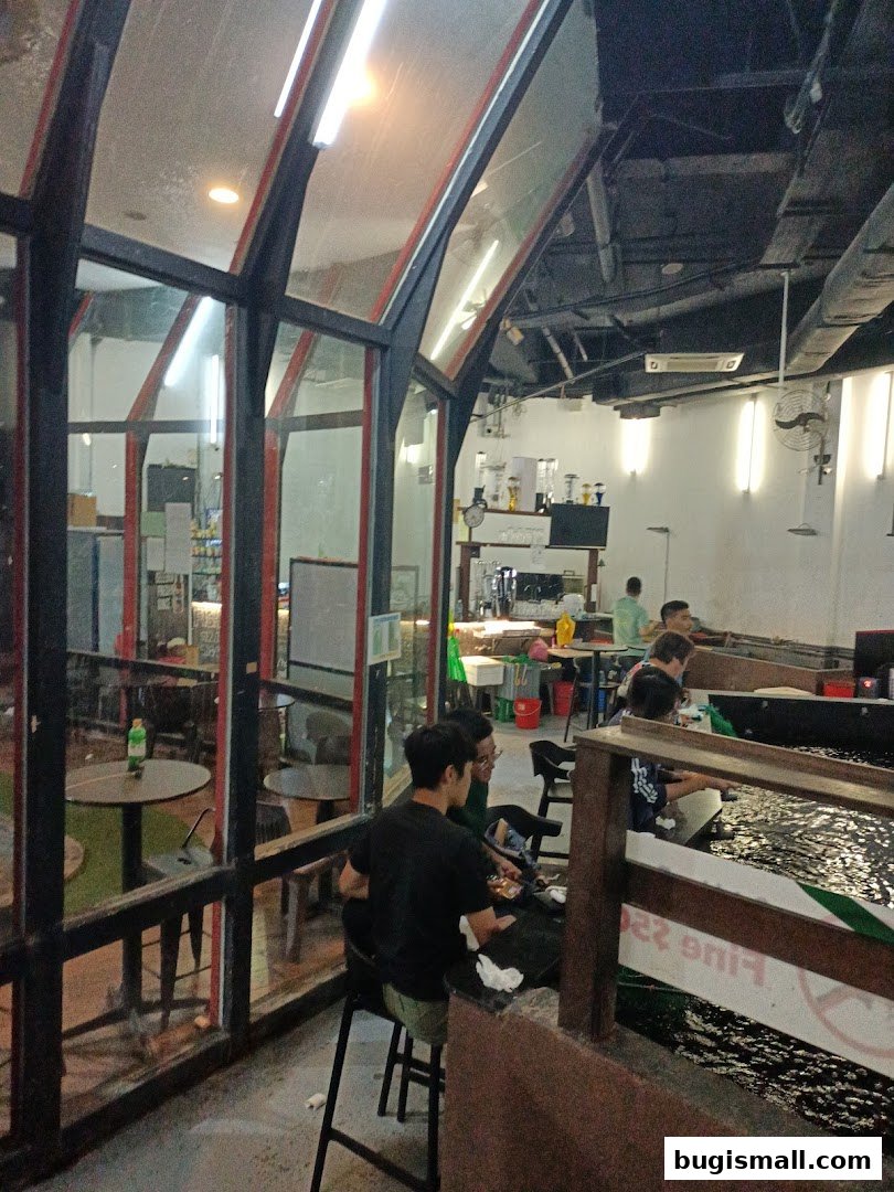 People dining at tables inside a restaurant with large glass windows and an indoor water feature.