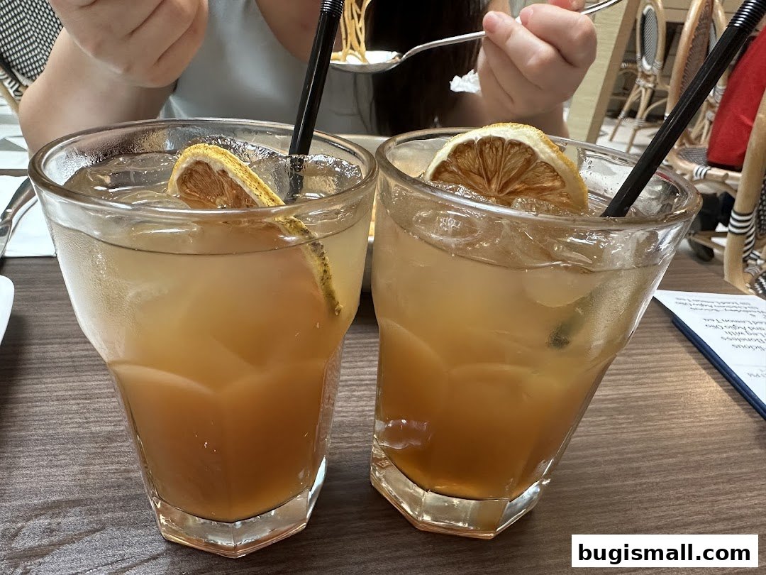 Two refreshing iced drinks with lemon slices and straws on a wooden table.