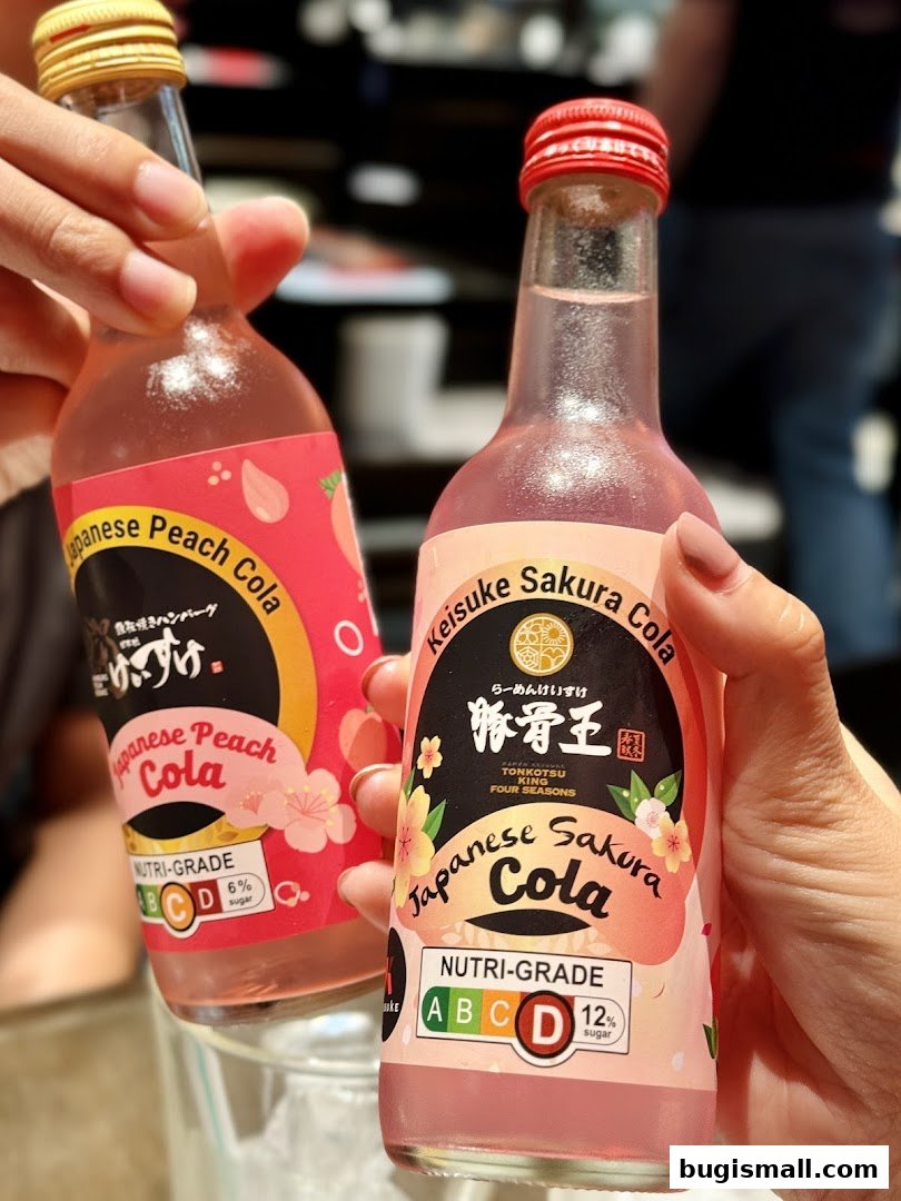 Two hands hold bottles of Japanese Peach Cola and Sakura Cola.