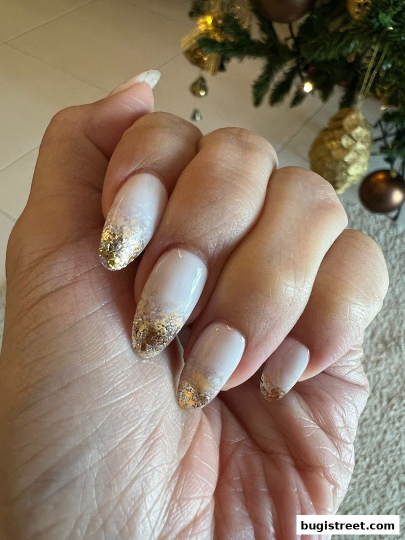 A close-up of a hand with elegant white and gold foil accent nails.