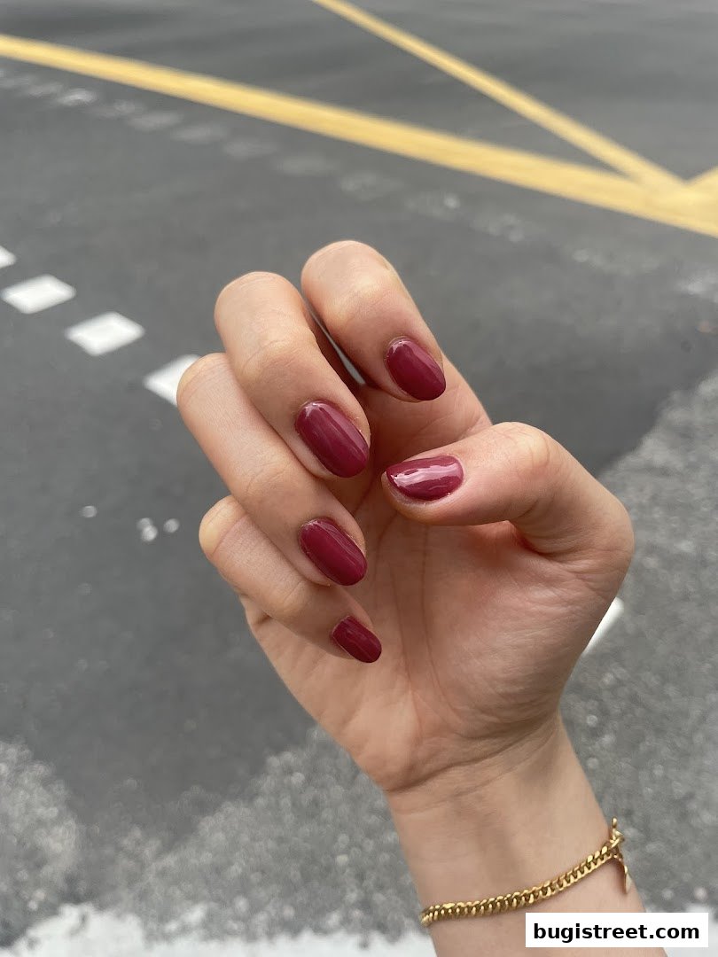 A hand with perfectly manicured nails painted in a deep berry shade, showcasing a stylish gold bracelet.