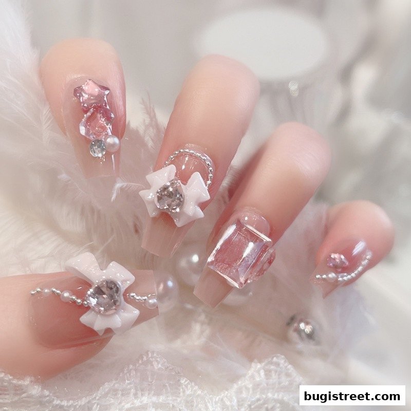 Close-up of hands with elaborate, bejeweled nail art featuring bows, gems, and pearls.