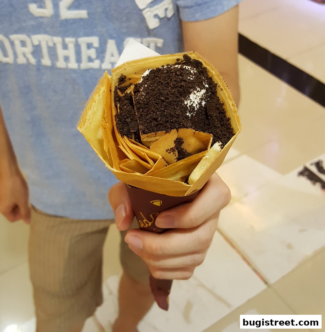 A person holds a delicious crepe filled with cream and cookie crumbles.