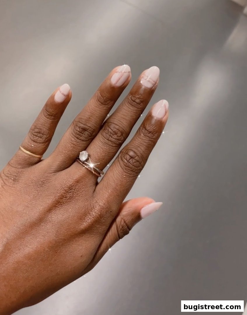 A close-up of a hand with light pink nails featuring subtle gold line accents and rings.
