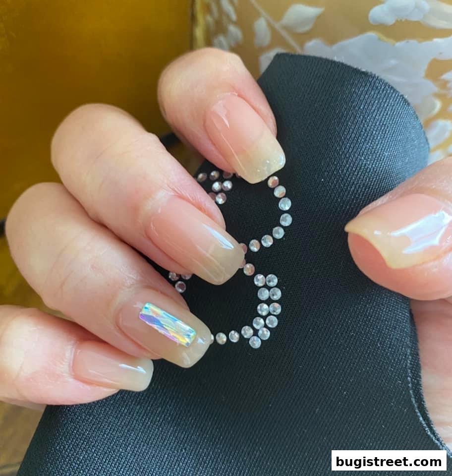 Close-up of a hand with natural-looking, glossy nails adorned with subtle rhinestones.