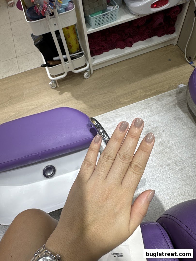 A person's hand with freshly painted neutral-toned nails in a nail salon.