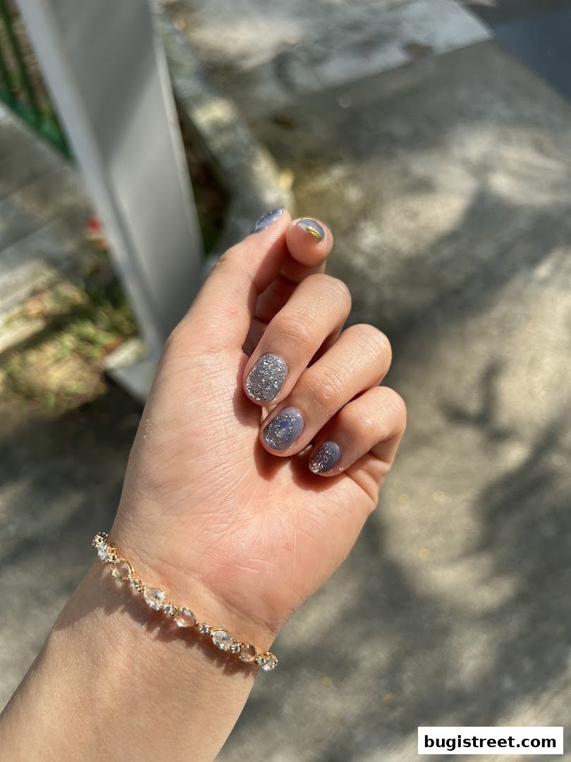 A hand with stylish grey and glittery nails and a delicate bracelet.