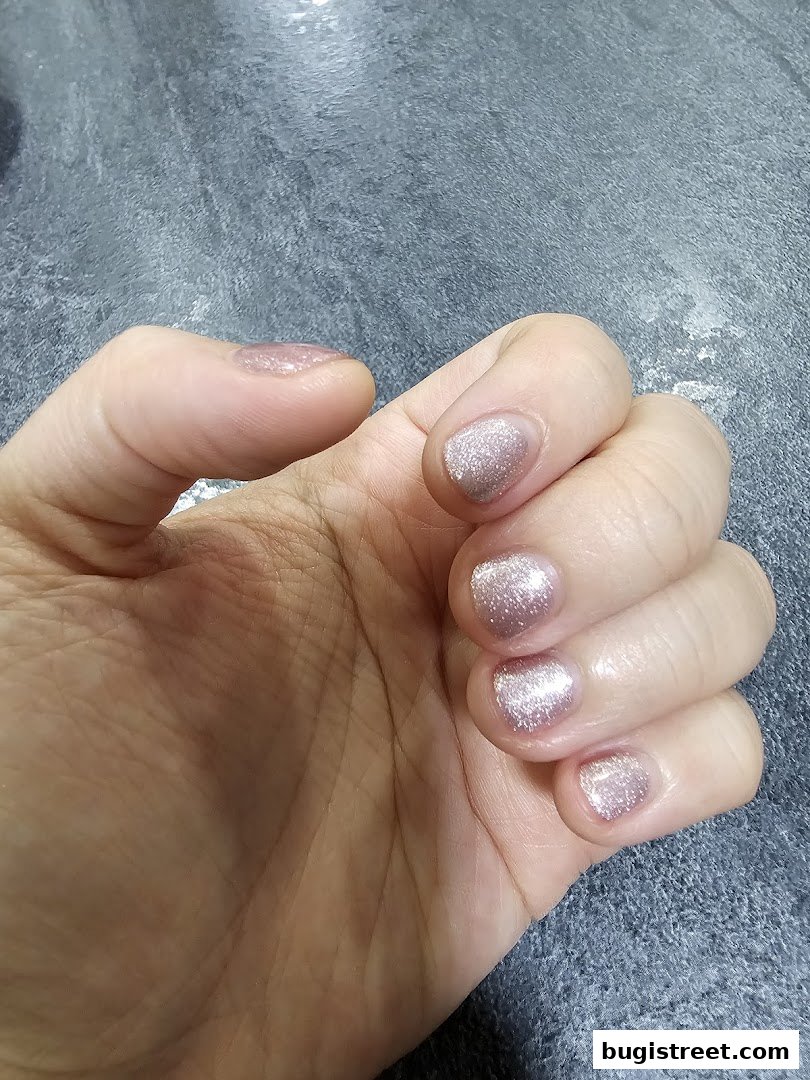 A close-up shot of a hand with short, neatly manicured nails painted with a shimmering rose gold polish.