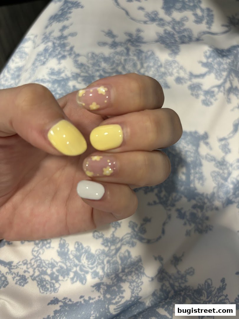 A close-up of a hand with yellow and floral-designed nails against a blue and white patterned background.
